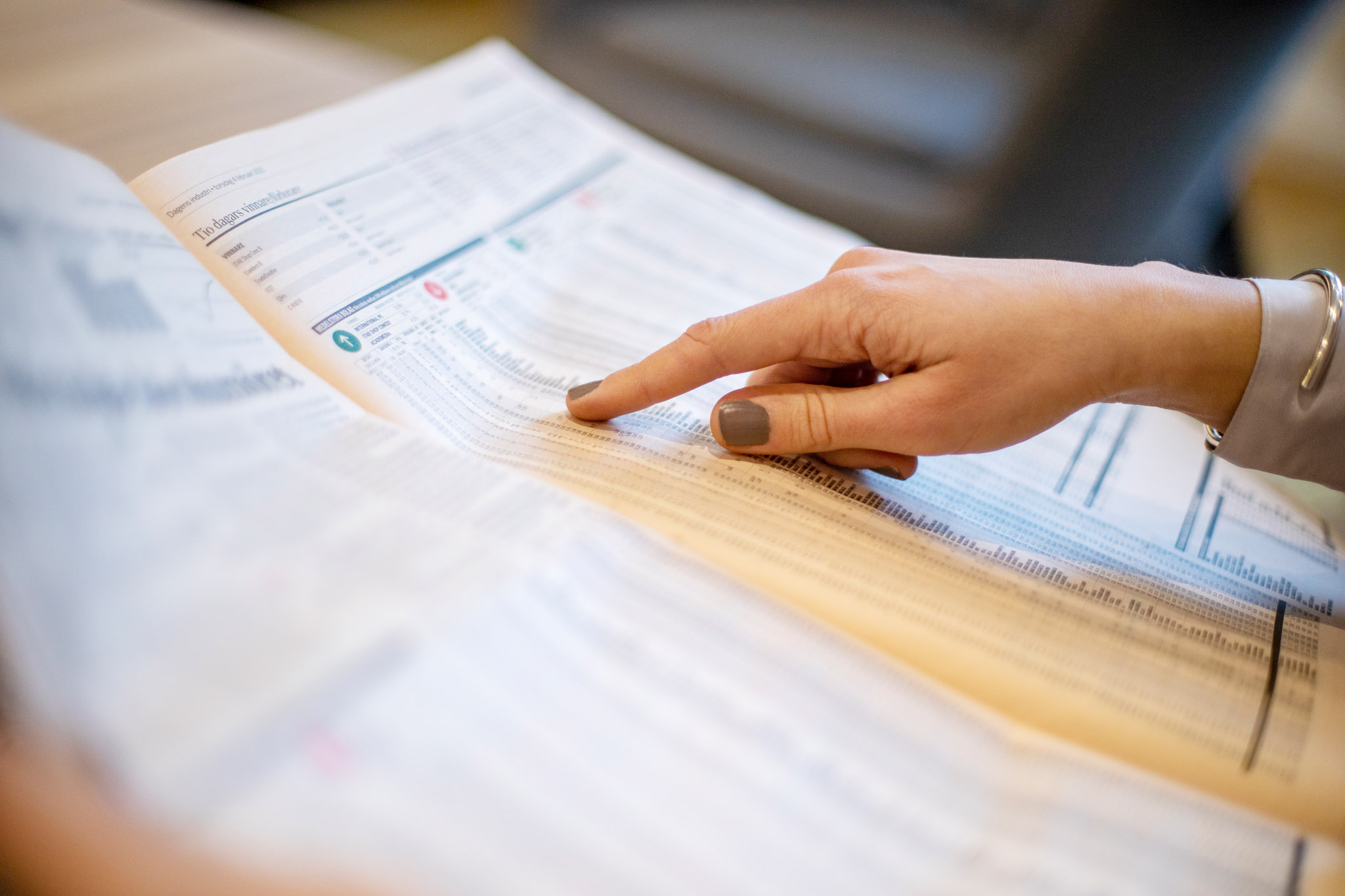 Hand pointing at stock exchange numbers in Swedish financial newspaper